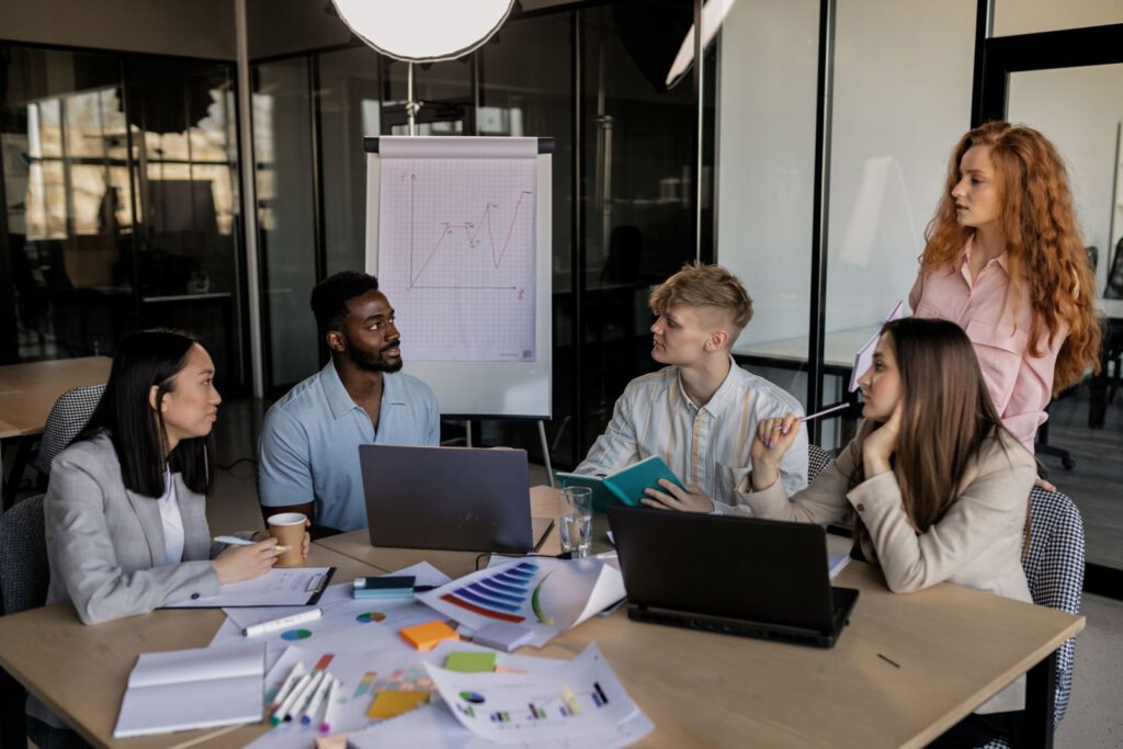 Colleagues around a meeting table reviewing charts with laptops
