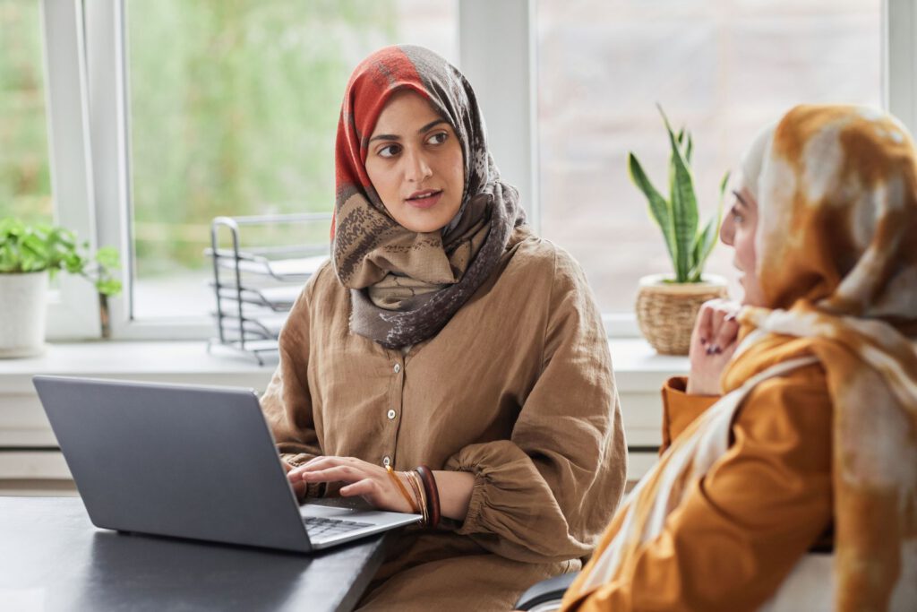 Two colleagues talking at a desk with a laptop