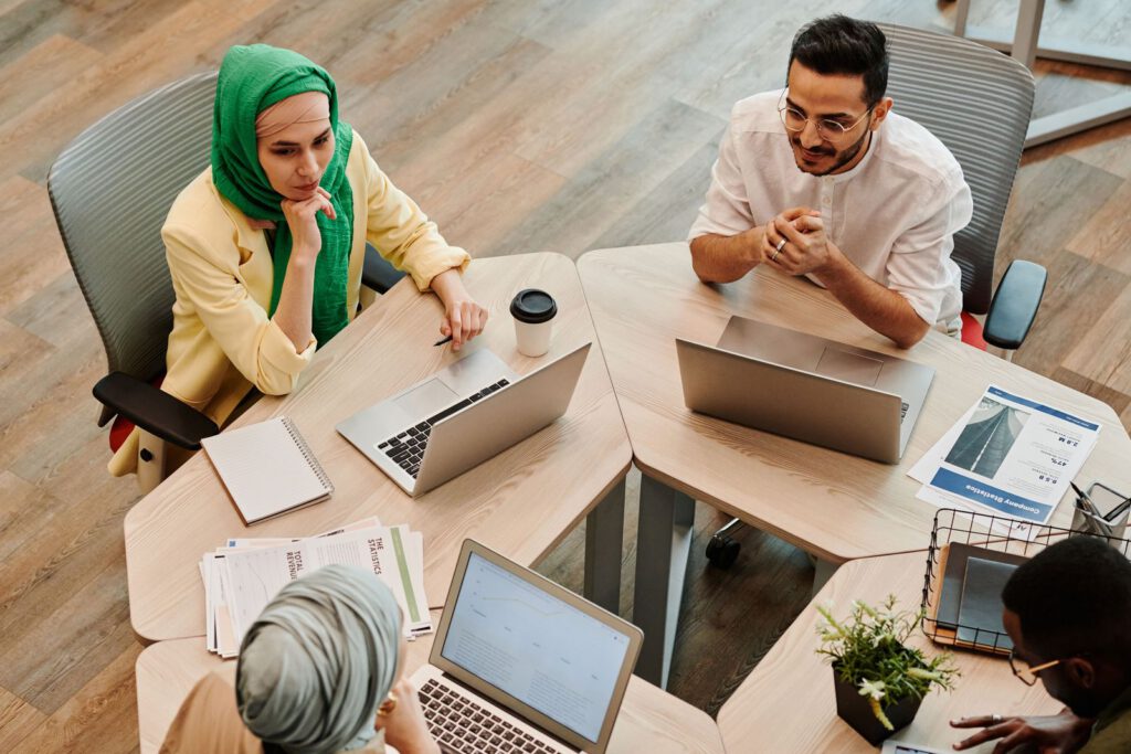 Overhead view of colleagues working at laptops around shared desks