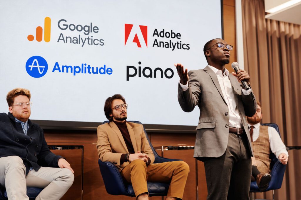 Speaker on stage in front of a screen showing analytics platform logos