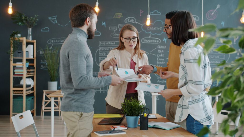 Team discussing printouts in front of a chalkboard wall