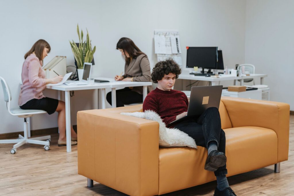 Team members working in a relaxed office, one on a sofa with a laptop